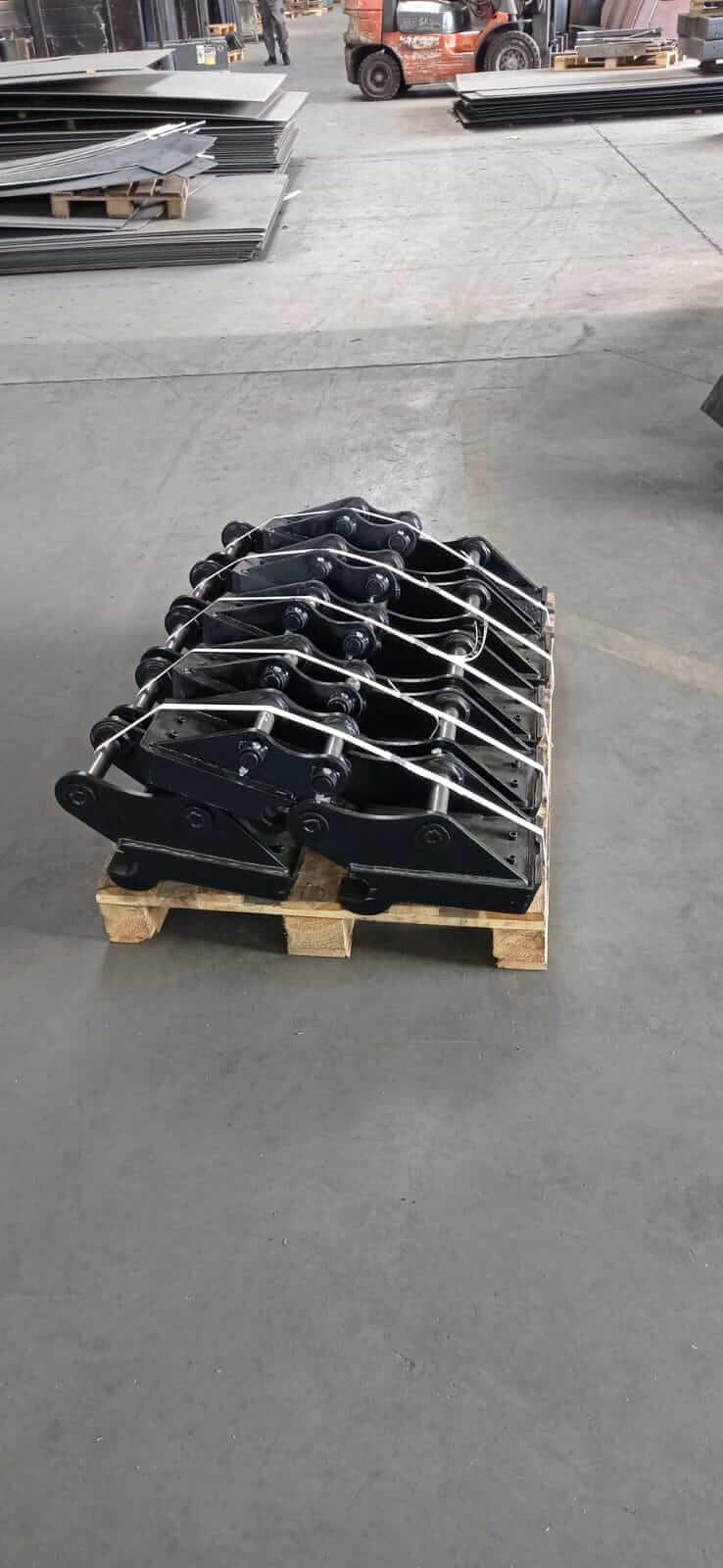Pomalowane szybkozłącza przypięte pasami do palety, w tle zapas blach.